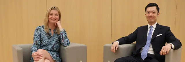 Ein Mann und eine Frau sitzen auf Stühlen, teilen sich eine Schüssel mit Essen und unterhalten sich.