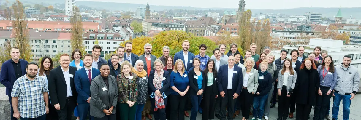 A diverse group of people is posing together on a rooftop in front of the cityscape of Heilbronn. The group represents the attendees of the Global Technology Forum 2024.