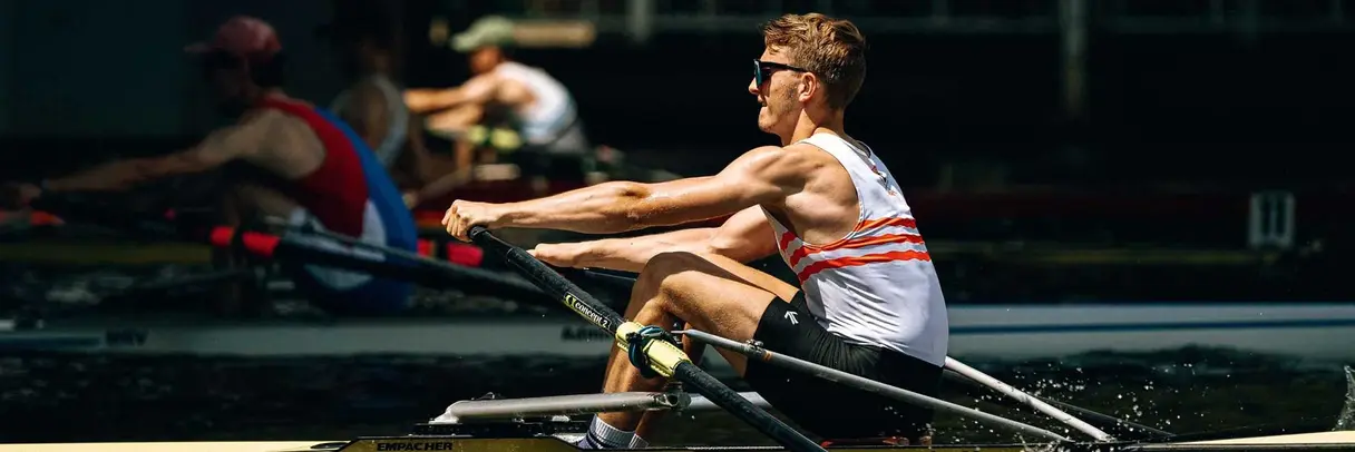 [Translate to German:] young, muscly man rowing fast on a river