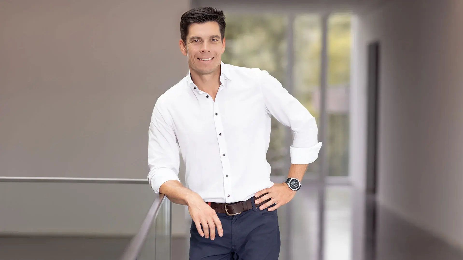 a man in a white shirt and dark pants leaning against a railing