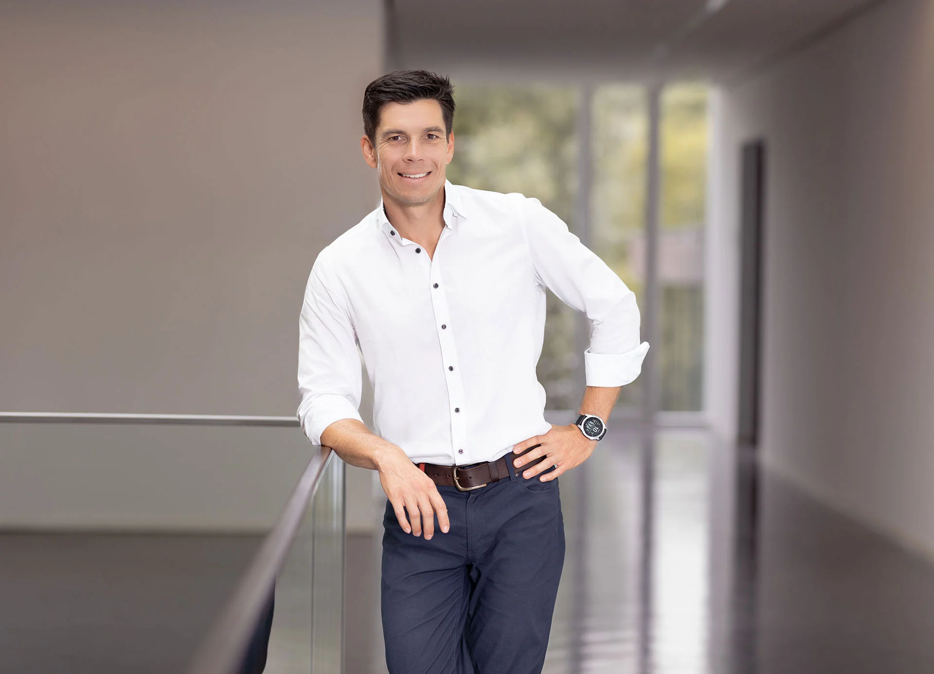 [Translate to German:] a man in a white shirt and dark pants leaning against a railing