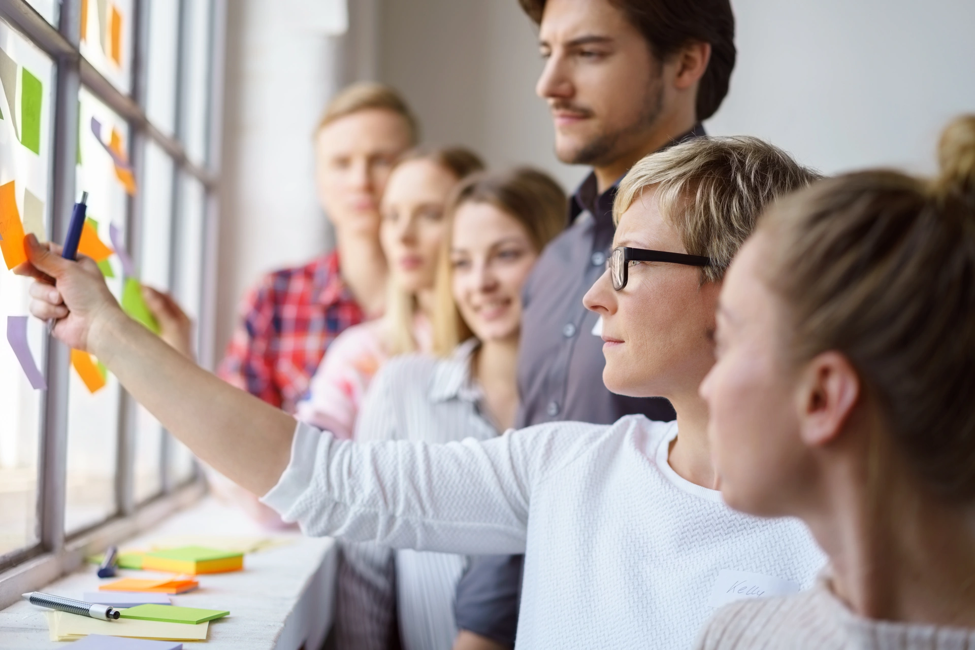 Eine Gruppe von Personen versammelt sich um ein mit bunten Haftnotizen bedecktes Fenster, diskutiert Ideen und arbeitet zusammen.