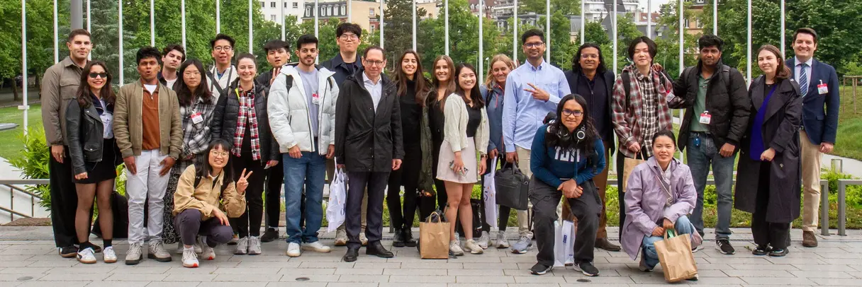 [Translate to German:] A group of diverse young people standing in front of a row of European flags
