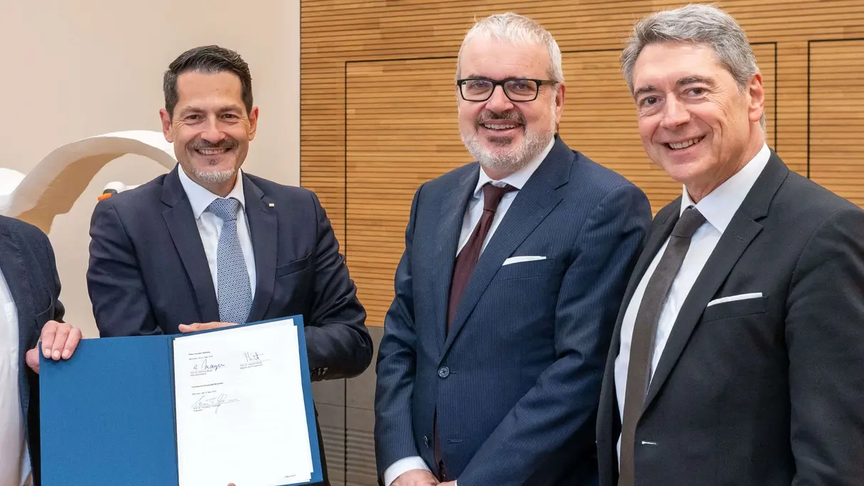 Eine Gruppe von Professoren in Businesskleidung präsentiert einen unterschriebenen Vertrag.