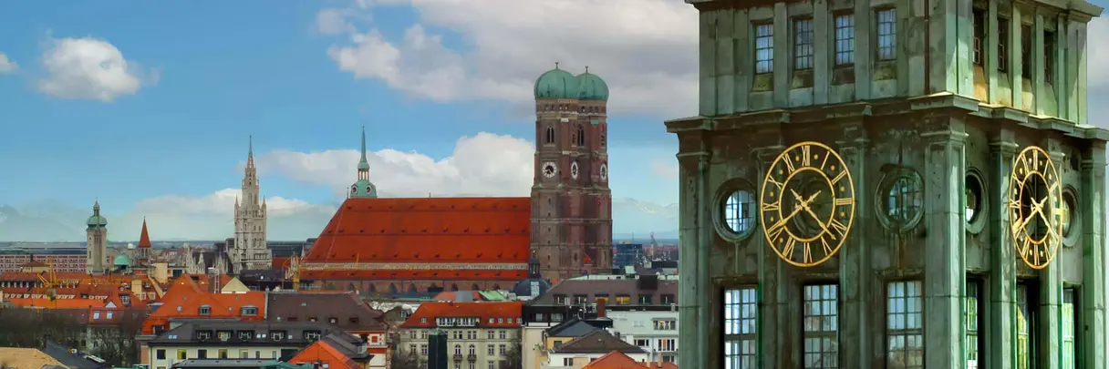 [Translate to German:] Ach church with two bell towers in the background, a green tower with a golden clock in the front