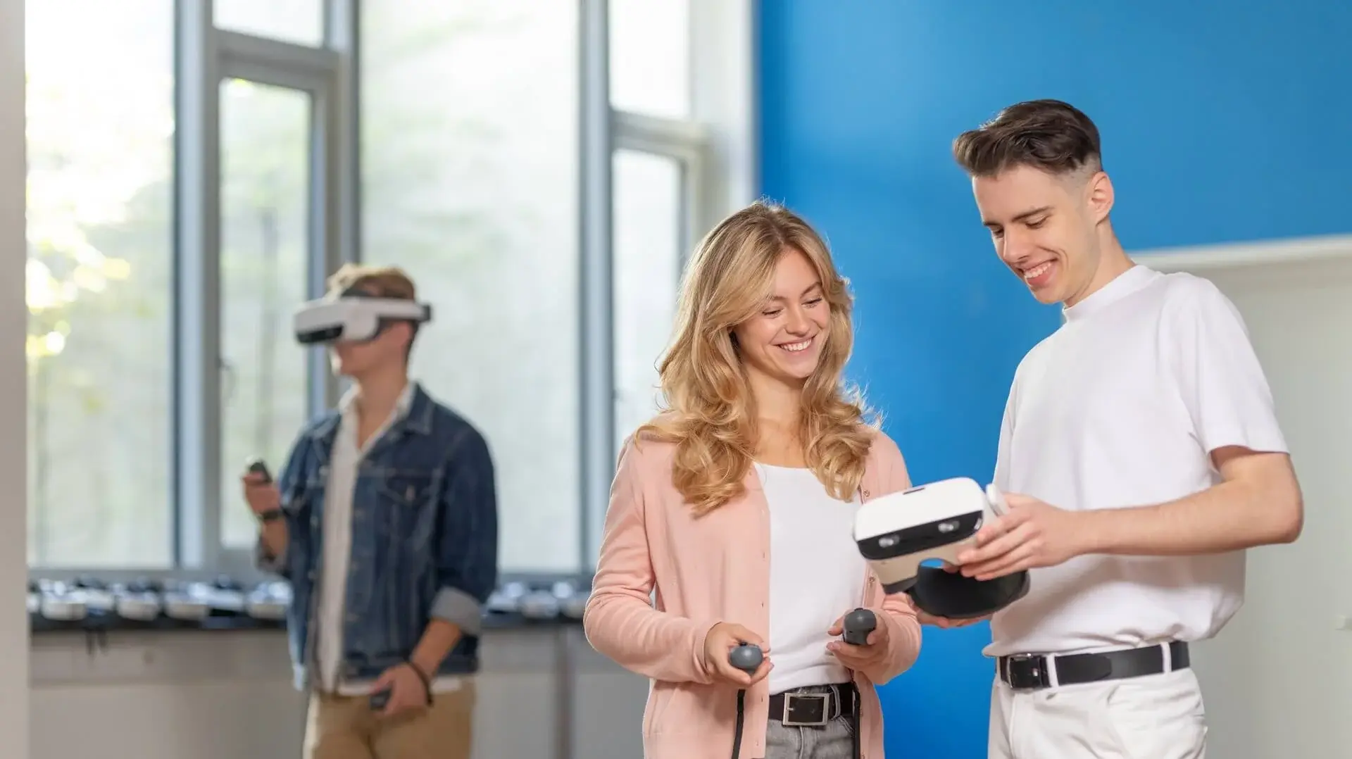 Zwei Studenten, die auf ein Tablet schauen, und ein Mann, der eine VR im Hintergrund benutzt